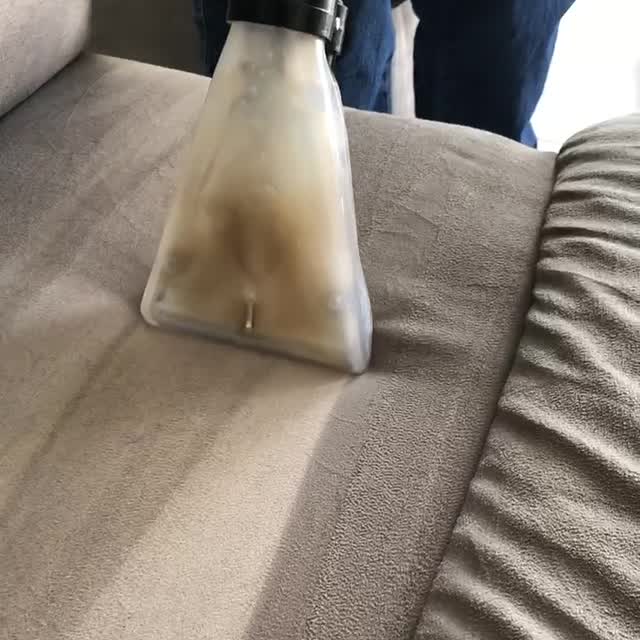 La boquilla de extracción transparente pasando por el asiento de un sofá y aspirando el agua sucia.